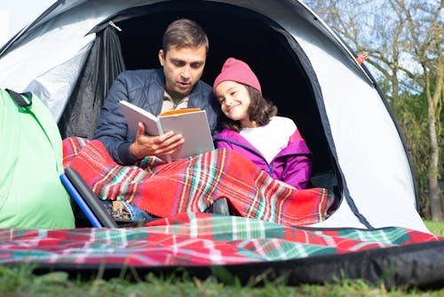 Father and Daughter Reading a Book while Sitting Inside the Tent